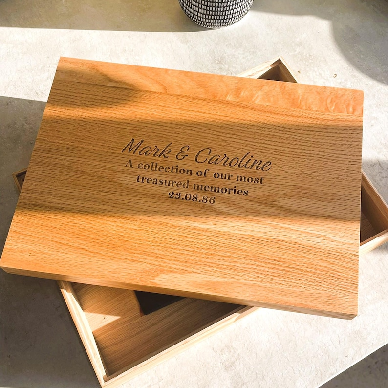 Pode incluir: Caixa de lembran&ccedil;as de madeira castanha clara com tampa aberta. A tampa &eacute; gravada com os nomes "Mark & Caroline", a frase "A collection of our most treasured memories" e a data "23.08.86". A caixa &eacute; de madeira.