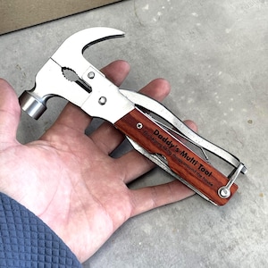 May include: A multi-tool featuring a hammer, pliers, and knife. The tool has a stainless steel finish with a wooden handle. The text "Daddy's Multi Tool" is engraved on the handle, along with the phrase "For helping fixing things around the house."