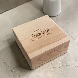 Peut inclure: Une boîte carrée en bois clair avec une finition lisse. Le couvercle est gravé avec le texte Mr & Mrs Fenwick 30 years & counting dans une police marron foncé. La boîte présente un grain de bois visible et un design simple et épuré.