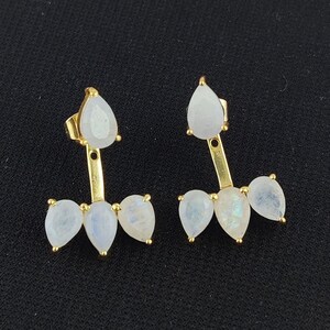Pode incluir: Um par de brincos de ouro com três pedras de lua em forma de lágrima em cada brinco. Os brincos são projetados para serem usados na parte superior da orelha.
