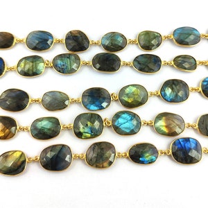 Puede incluir: Una hebra de cadena dorada con piedras preciosas de labradorita de forma ovalada. Las piedras son una mezcla de azul oscuro, verde y dorado.