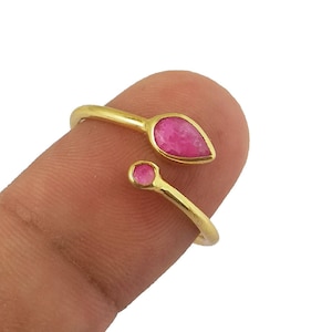 Puede incluir: Un anillo de oro con dos piedras preciosas rosas. El anillo está diseñado para envolverse alrededor del dedo.
