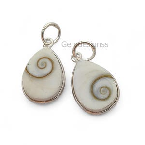Puede incluir: Dos colgantes en forma de lágrima con borde plateado. Cada colgante presenta un diseño blanco con remolinos y una espiral marrón en el centro. Los colgantes tienen un pequeño lazo en la parte superior para colgar. El texto "Gendesignss" es visible.