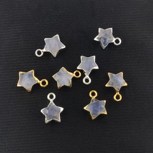 May include: A collection of star-shaped charms with a light blue stone center. Some charms have a silver-colored metal border and loop, while others have a gold-colored border and loop. The charms are displayed on a black surface.
