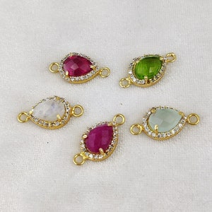 May include: Five gold-tone teardrop-shaped connector charms with clear, white, green, and red gemstones. Each charm is surrounded by a row of clear cubic zirconia stones.