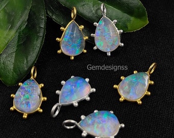 May include: A collection of teardrop-shaped opal pendants. The opals display iridescent colors and are set in gold and silver metal settings. The pendants have a textured, spiky border and are displayed on a black surface with green leaves.