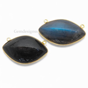 May include: Two marquise-shaped gemstone pendants. One is a deep black, the other a dark blue with iridescent flashes. Both are set in gold-colored bezels with small loops for attaching to jewelry. The pendants are displayed on a white background.