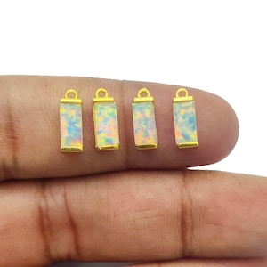 Peut inclure: Quatre pendentifs en forme de barre plaqués or avec des pierres d'opale blanche. Chaque pendentif a une boucle en haut pour l'attacher à une chaîne ou un cordon.