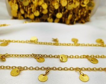 May include: Two gold chains with small round gold charms hanging from them. The chains are on a white fabric background.