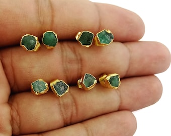 May include: A set of six gold-plated earrings featuring raw emerald gemstones. Each earring has a unique shape and size, showcasing the natural beauty of the emerald.