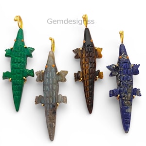 May include: Four crocodile-shaped pendants with gold-toned bails, carved from malachite, labradorite, tiger's eye, and lapis lazuli. Each gemstone alligator features small orange accents for eyes and a textured, scaled back design.