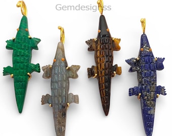 May include: Four crocodile-shaped pendants with gold-toned bails, carved from malachite, labradorite, tiger's eye, and lapis lazuli. Each gemstone alligator features small orange accents for eyes and a textured, scaled back design.