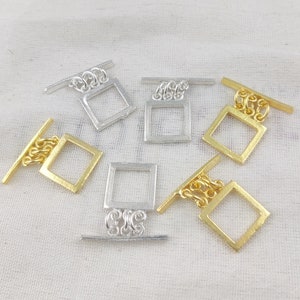 May include: Six silver and gold metal toggle clasps with a square design. The clasps have a chain link and a sliding bar.