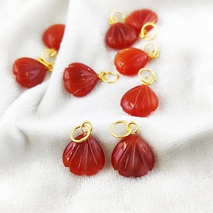 May include: A set of ten red carnelian gemstone flower charms with gold-toned jump rings. The charms are ideal for jewellery making or adding a touch of elegance to any project.