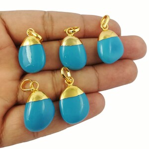 May include: Five turquoise-colored pendants with gold-colored caps and loops. The pendants are teardrop-shaped and have a smooth, polished surface. The gold caps add a touch of elegance to the pendants.