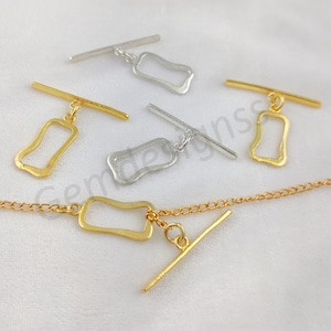 May include: Four gold and silver toggle clasps with a chain. The clasps are made of metal and have a rectangular shape with a rounded edge. The chain is made of metal and has a link design.