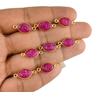 May include: Eight gold-toned oval-shaped connector charms with a carved eye design and a pink gemstone.