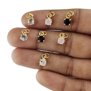 Può includere: Sei ciondoli in oro con pietre preziose di diversi colori. I ciondoli sono rotondi e hanno un anello nella parte superiore per essere attaccati a una collana o un braccialetto. Le pietre preziose sono acquamarina, quarzo rosa, onice nero e pietra di luna bianca.