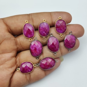 May include: Eight pink oval gemstone connector charms with gold and black metal accents. The charms have a faceted finish and are perfect for jewelry making.
