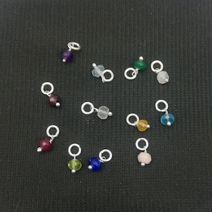 Puede incluir: Surtido de 12 abalorios de piedras preciosas con anillas de salto de plata. Los abalorios presentan varios colores, incluyendo morado, rojo, blanco, verde, amarillo, azul y rosa.