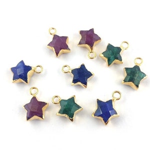 以下が含まれることがあります： 紫、青、緑など、さまざまな色の星型の宝石チャームのコレクション。各チャームは金色の縁取りと、ジュエリーに取り付けるための小さなループが付いています。宝石はファセットカットされています。