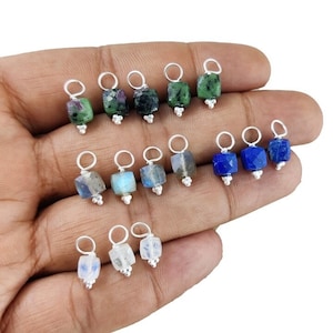 Puede incluir: Un conjunto de 12 colgantes de plata con diferentes cuentas de piedras preciosas. Las cuentas son de forma cuadrada y vienen en verde, azul y blanco.