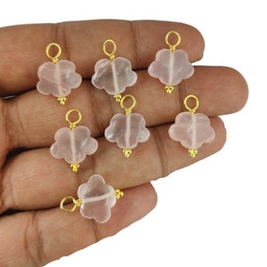 Op de afbeelding: Zeven roze rozenkwarts bloembedels met goudkleurige accenten. Elke bedel heeft een lus om aan sieraden te bevestigen.