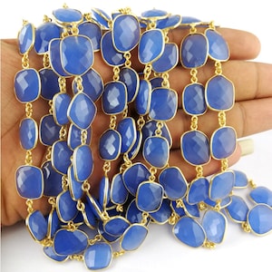 May include: A strand of blue chalcedony gemstone beads with gold-toned metal accents. The beads are faceted and have a square shape. The strand is approximately 18 inches long.