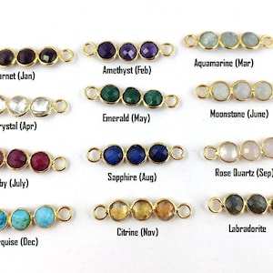Op de afbeelding: Twaalf goudkleurige connector charms, elk met drie facetgeslepen edelsteen kralen. De charms zijn gelabeld met de geboortesteen voor elke maand van het jaar, beginnend met Granaat (januari) en eindigend met Turquoise (december).