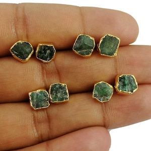 Puede incluir: Ocho pendientes de piedra preciosa verde esmeralda con engastes chapados en oro. Los pendientes se muestran en una mano.