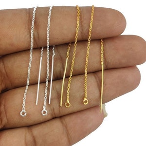 Könnte beinhalten: Vier Ohrringketten, zwei silber und zwei gold, mit Sprungringen oben und geraden Enden. Die Ketten werden auf einer Hand gezeigt.