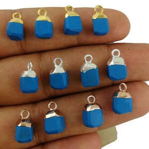 May include: A collection of 12 blue gemstone pendants with gold and silver accents. The pendants are in the shape of a rectangle with a slightly rounded top and bottom. They are perfect for jewelry making or crafting.