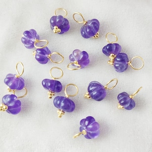 May include: A collection of 12 purple amethyst gemstone charms with gold accents. Each charm features a flower-shaped amethyst stone with a gold loop for attaching to jewelry.
