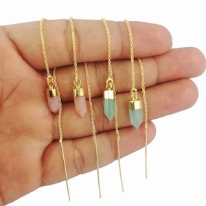 May include: Four pairs of gold chain earrings with crystal charms. Two pairs feature light pink crystal charms and two pairs feature light green crystal charms.