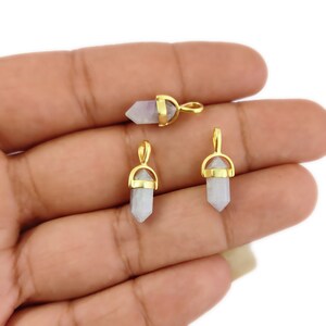 May include: Three gold-toned crystal point pendants with a loop for attaching to a necklace or bracelet. The crystals are a light purple colour.