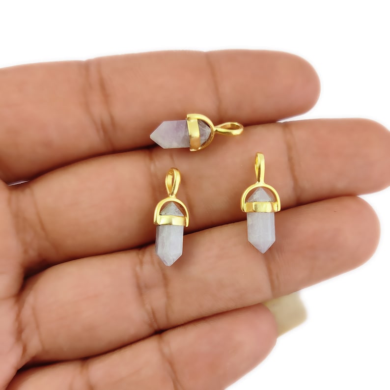 May include: Three gold-toned crystal point pendants with a loop for attaching to a necklace or bracelet. The crystals are a light purple colour.