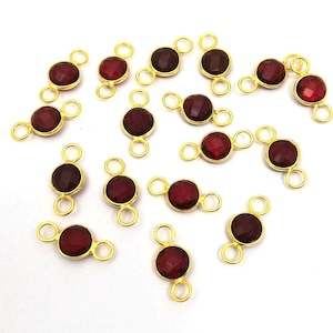 Op de afbeelding: Een groep van 18 gouden edelsteenverbinders met ronde rode edelstenen. Elke connector heeft twee lussen om aan sieraden te bevestigen.