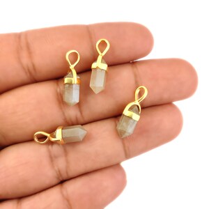 May include: Four gold-plated crystal point pendants in a light grey colour. The pendants are shaped like a point with a gold-plated loop at the top.