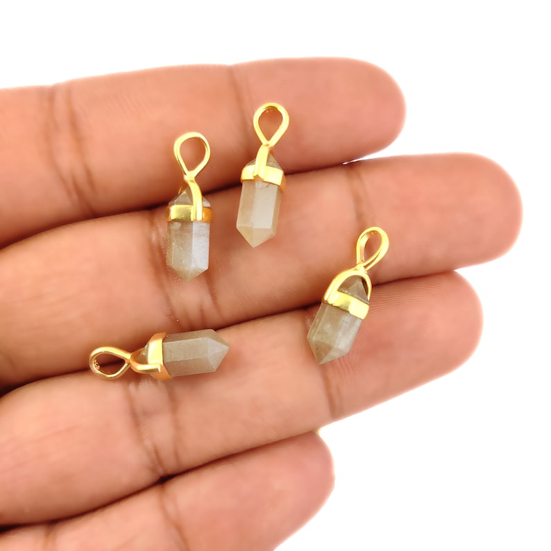 May include: Four gold-plated crystal point pendants in a light grey colour. The pendants are shaped like a point with a gold-plated loop at the top.