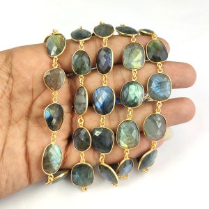 May include: A strand of gold-plated labradorite gemstone beads. The beads are oval-shaped and have a dark blue, green, and gold iridescent sheen.