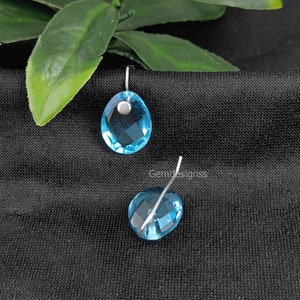 May include: A pair of blue gemstone earrings with silver wire loops. The gemstones are faceted and have a light blue color.