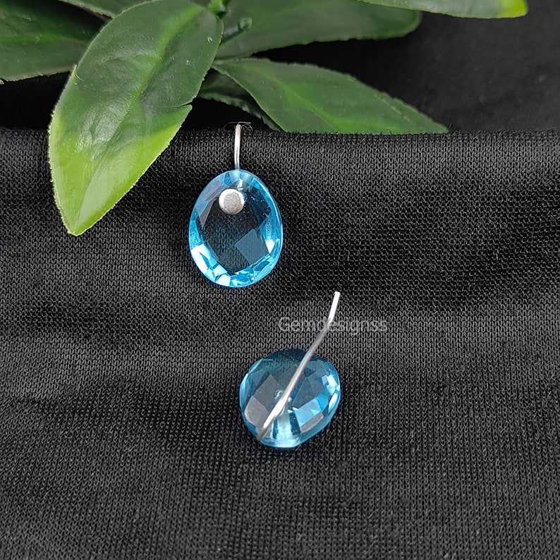 May include: A pair of blue gemstone earrings with silver wire loops. The gemstones are faceted and have a light blue color.