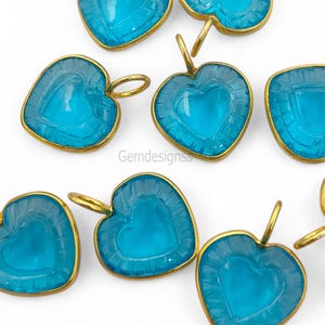 May include: A collection of heart-shaped pendants in a light blue colour, each with a gold-coloured frame. The pendants feature a heart design carved within and a small loop for suspension. The text "Gemdesignss" is visible.