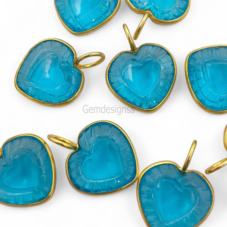 May include: A collection of heart-shaped pendants in a light blue colour, each with a gold-coloured frame. The pendants feature a heart design carved within and a small loop for suspension. The text "Gemdesignss" is visible.