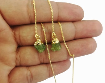 May include: A pair of gold chain earrings with green gemstone drops. The earrings are long and dangle from the earlobe.