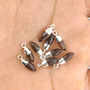 Puede incluir: Un grupo de ocho colgantes de piedra preciosa de cuarzo ahumado con lazos de plata. Los colgantes son facetados y tienen una forma puntiaguda.