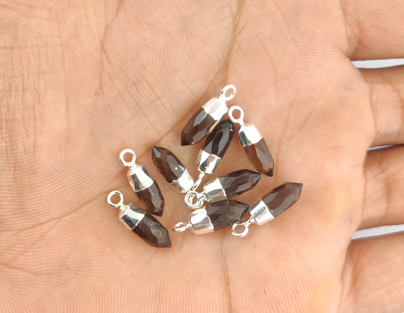 Puede incluir: Un grupo de ocho colgantes de piedra preciosa de cuarzo ahumado con lazos de plata. Los colgantes son facetados y tienen una forma puntiaguda.
