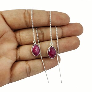 May include: A pair of silver chain earrings with red gemstone drops. The earrings are approximately 5 cm long.