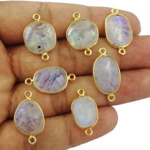Könnte beinhalten: Acht ovale Mondstein-Perlen mit goldfarbenen Metall-Verbindungsschlaufen. Die Perlen sind hellblau-grau mit irisierendem Schimmer.