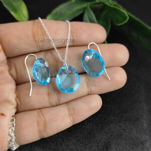 May include: A silver necklace and earrings set with a light blue gemstone pendant and matching earrings. The pendant and earrings are oval shaped.